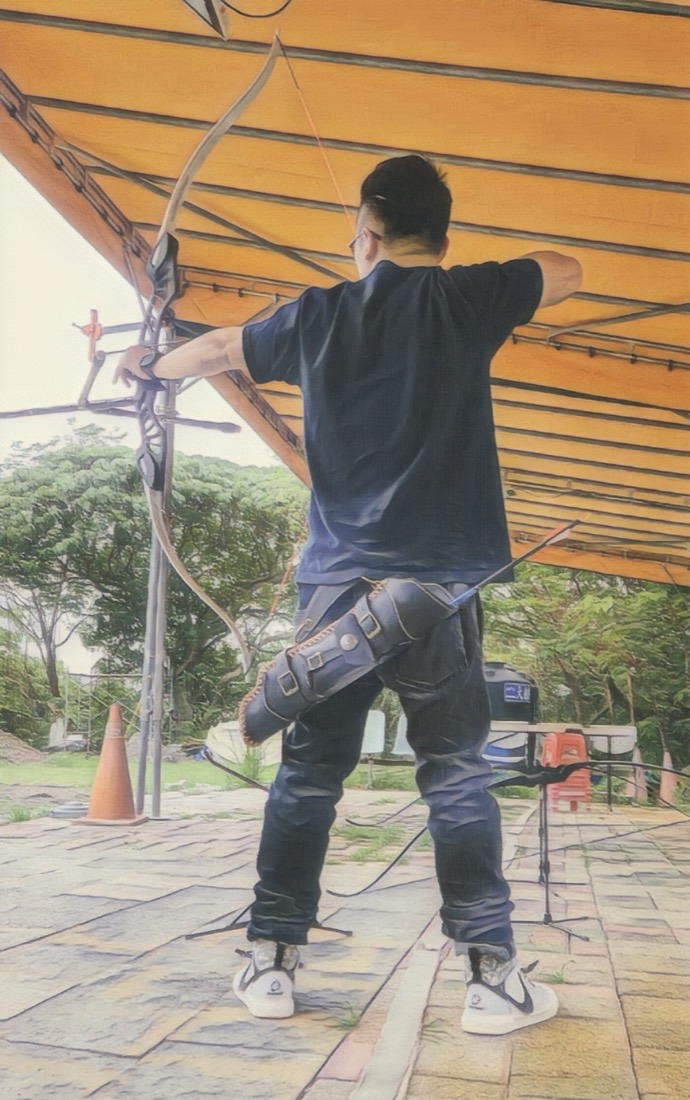 Ray at full draw with a recurve bow at an outdoor archery range